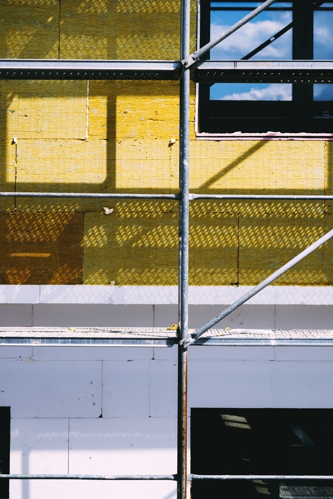 Isolation thermique jaune : rénovation de façade et échafaudage. Isolation thermique jaune de la façade en rénovation. L'échafaudage projette des ombres géométriques sur la laine minérale et le polystyrène blanc.