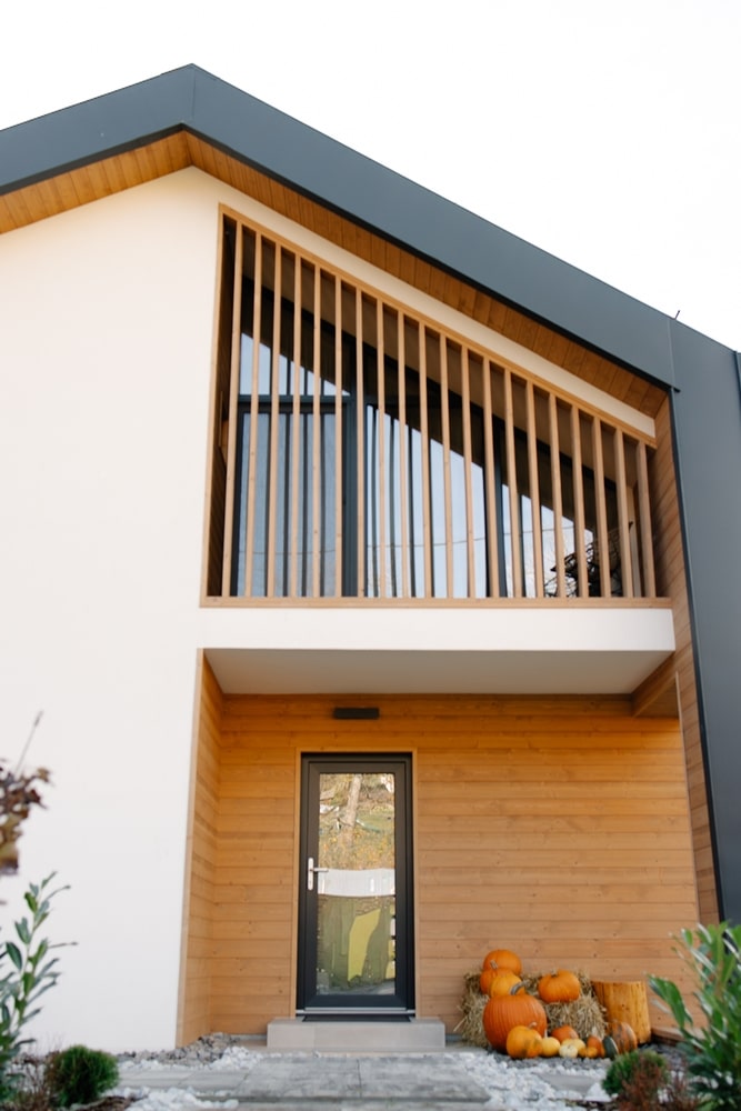 Maison Moderne en Bois : Design Contemporain et Déco Automne Entrée de maison moderne en bois et blanc avec décor automnal de citrouilles et balcon à claire-voie.